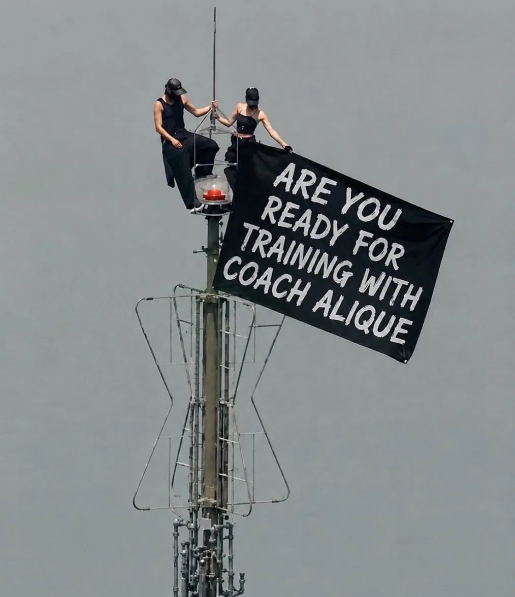 A banner reading 'Are you ready for training with Coach Alique' hung from a cell tower