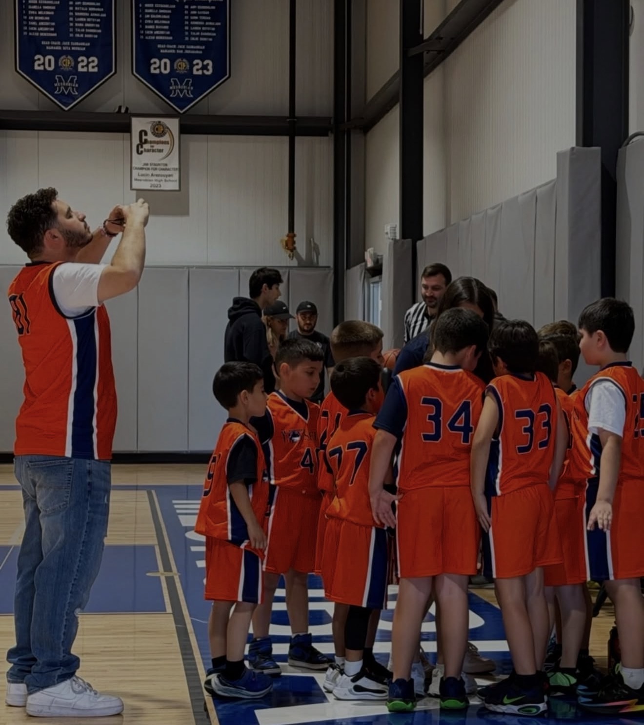 Coach huddled with a youth basketball team in orange jerseys during a game